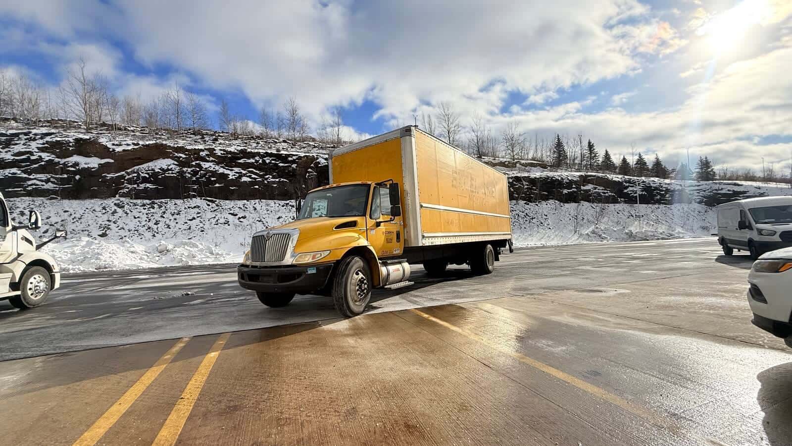Cobra's yellow box truck parked on an icy, snow-covered truck lot in bright winter sun.
