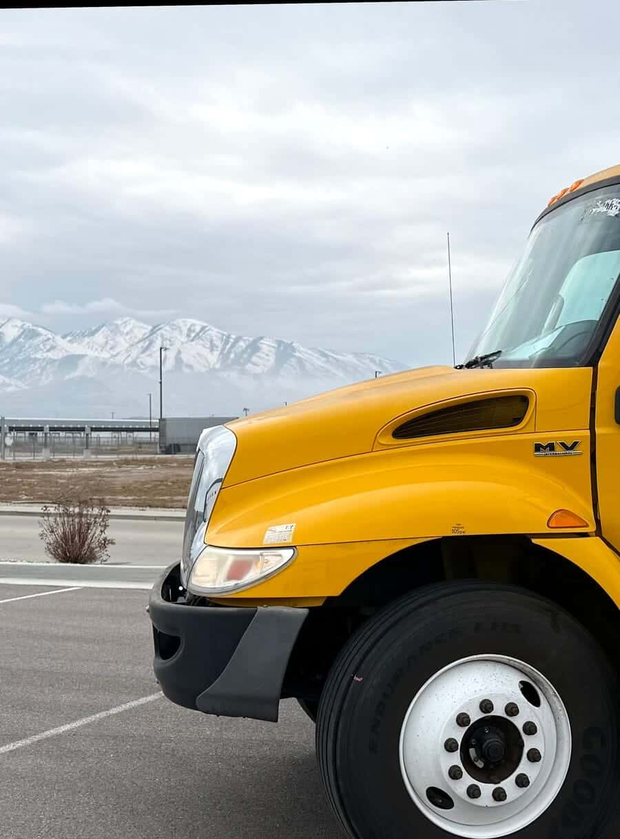 Cobra US Cargo's yellow International box truck parked under a wide sky, with snow-covered mountains behind it.