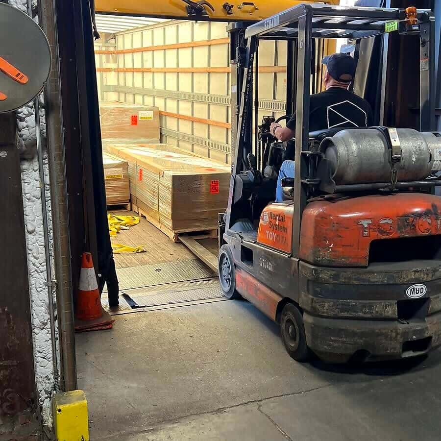 A forklift loads shrink-wrapped pallets of boxes into a box truck at a dock door, with e-track on the walls.